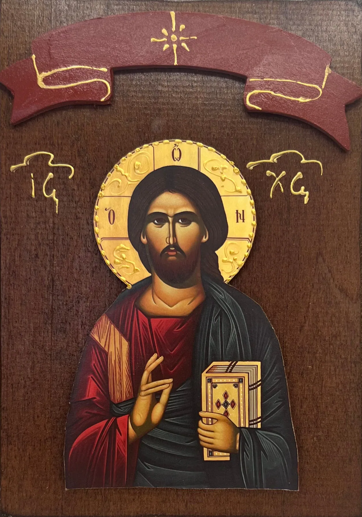 Drvena ikona Isusa Hrista Pantokratora - Hristos blagosilja i drži Jevanđelje, zlatni reljefni oreol sa slovima Ο ΩΝ, monogram IC XC, crvena drvena traka na pravougaonoj drvenoj dasci