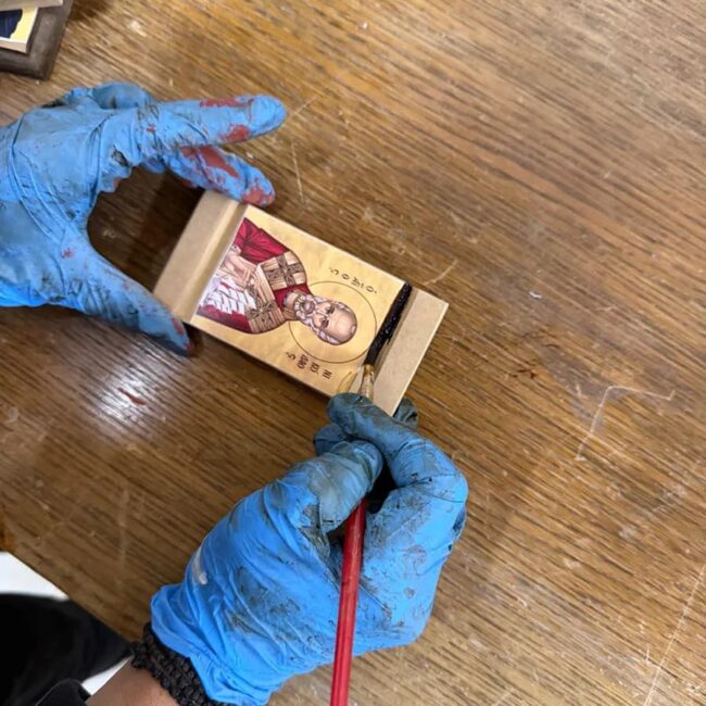 Umetnik ručno oslikava detalje na pravoslavnoj ikoni tankom četkicom.